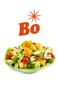 The image showcases a vibrant Chicken Supremes Salad on a green ceramic plate, topped with crispy breaded chicken pieces, fresh lettuce, cucumber slices, cherry tomatoes, carrots, and black olives. The salad is drizzled with creamy dressing, and bold red "Bo" lettering with a starburst graphic is displayed above. The background is pure white, emphasizing the colorful ingredients and the fresh appeal of the dish. Bojangles menu
