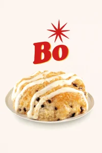 "A Bo-Berry Biscuit featuring a warm, soft biscuit topped with sweet glaze and filled with berries, all drizzled with white icing. The biscuit is placed on a white plate with the word 'Bo' in bold red letters and a starburst above it, set against a plain light-colored background. Bojangles  Menu